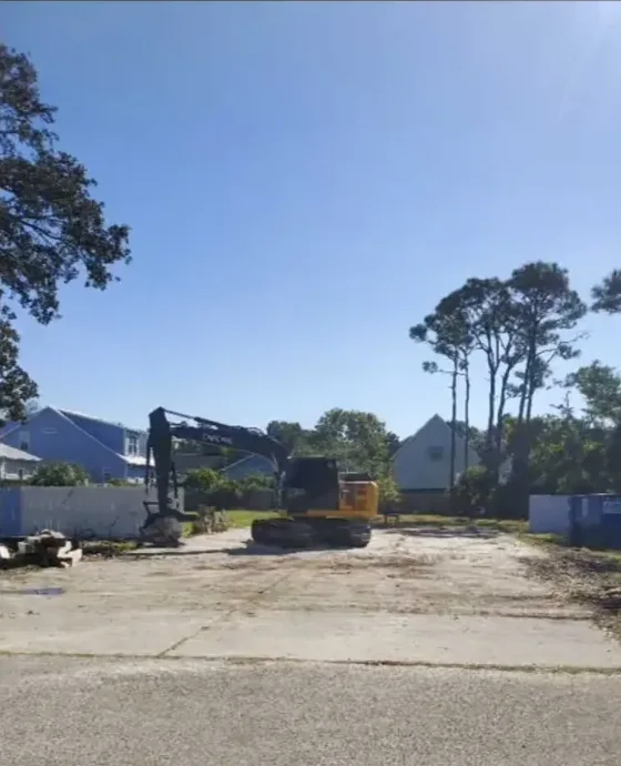 Excavator on a cleared homesite between houses after teardown and site prep near Wilmington, NC